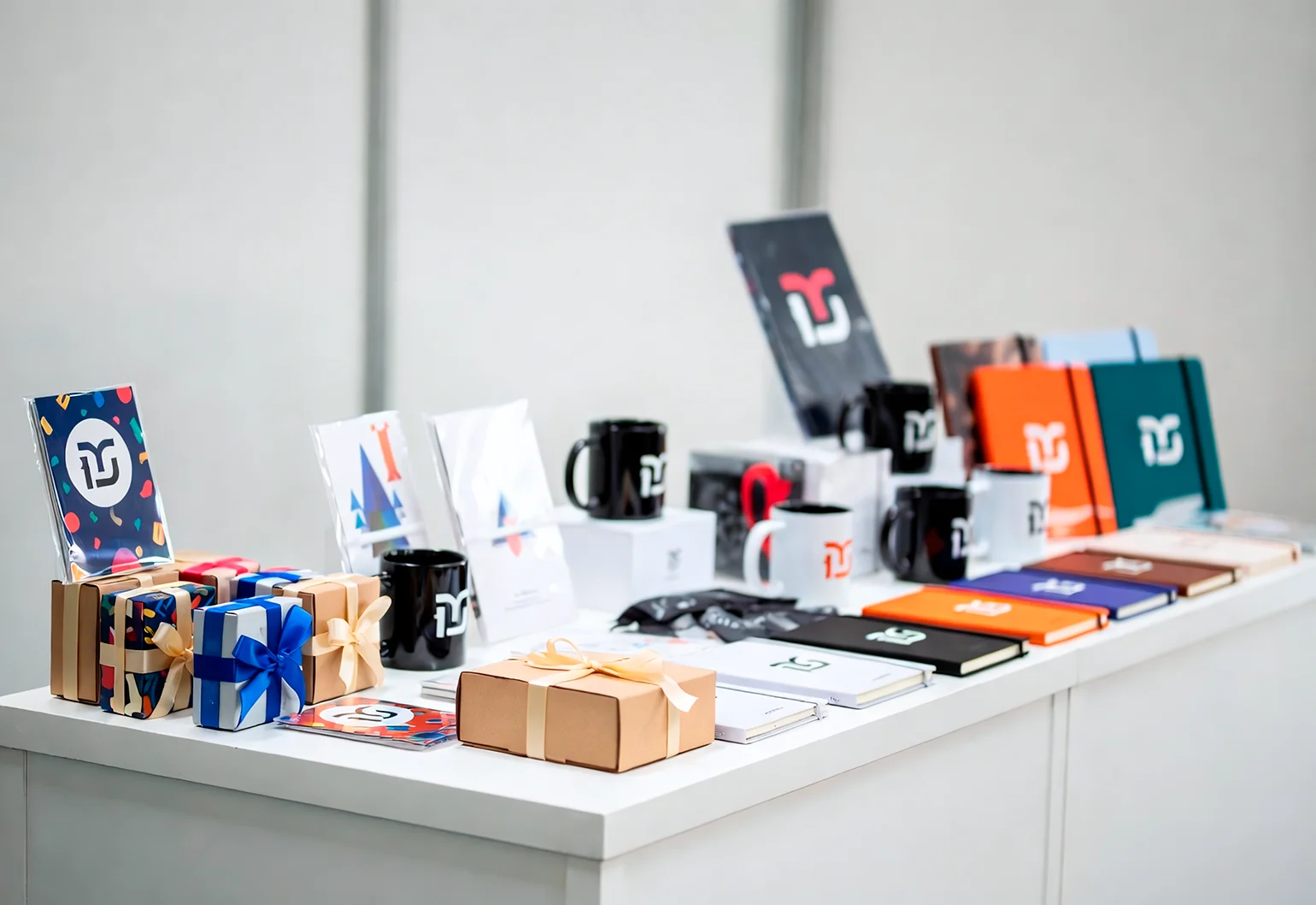 Подарочные наборы и мерч с логотипом бренда, разложенные на стойке стенда